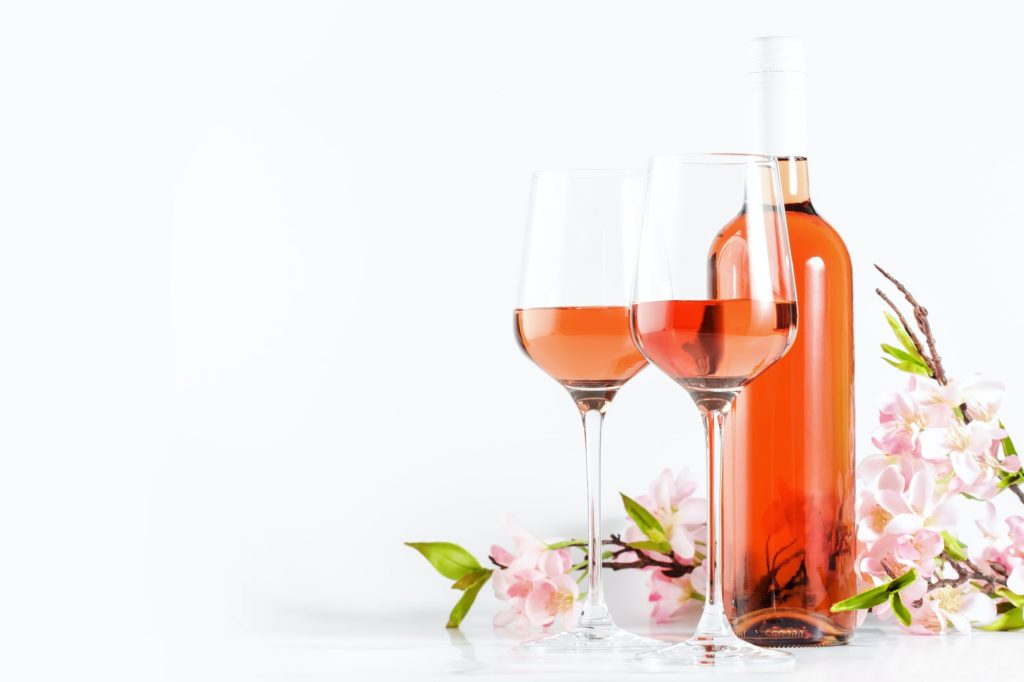 Rose wine glass with bottle on the white table and pink flowers